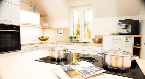 Moderne, helle Einbauküche mit Induktionskochfeld, Edelstahl-Töpfen und Kaffeemaschine.