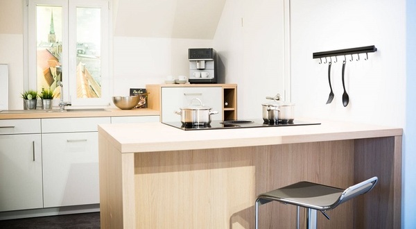 Moderne Einbauküche mit Kochinsel, Hängeregal und Kaffeemaschine, hell und einladend.