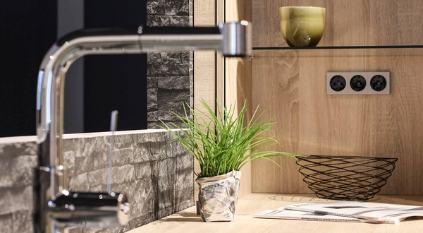 Moderne Küchenarbeitsplatte mit Wasserhahn, Dekopflanze, Steckdosen und Küchenaccessoires.